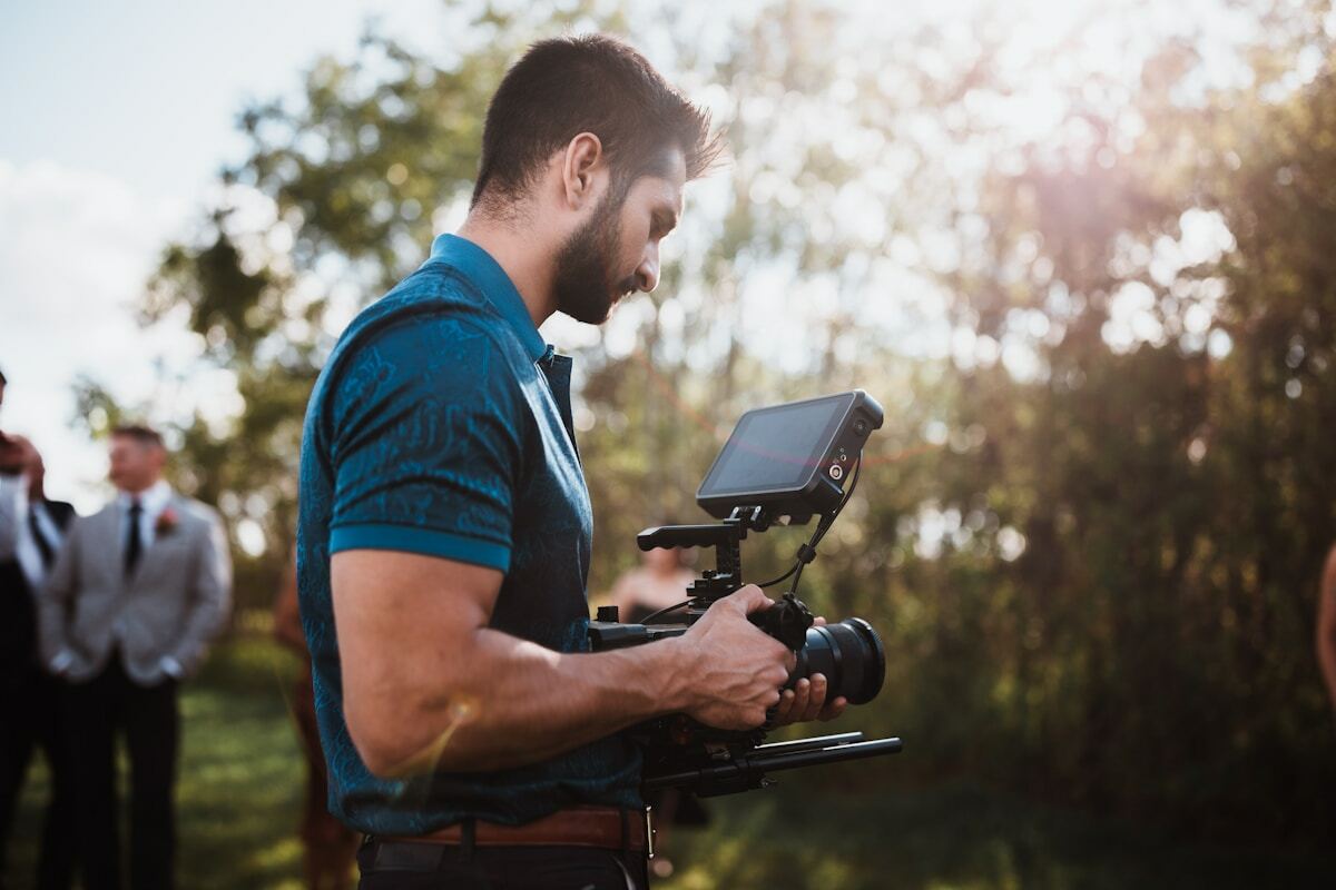 Homme barbu filmant avec une caméra professionnelle dans un environnement naturel.