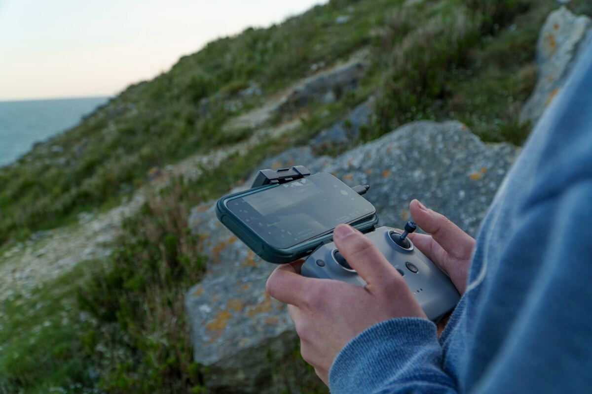 Personne tenant une manette de jeu vidéo dans un paysage montagneux.