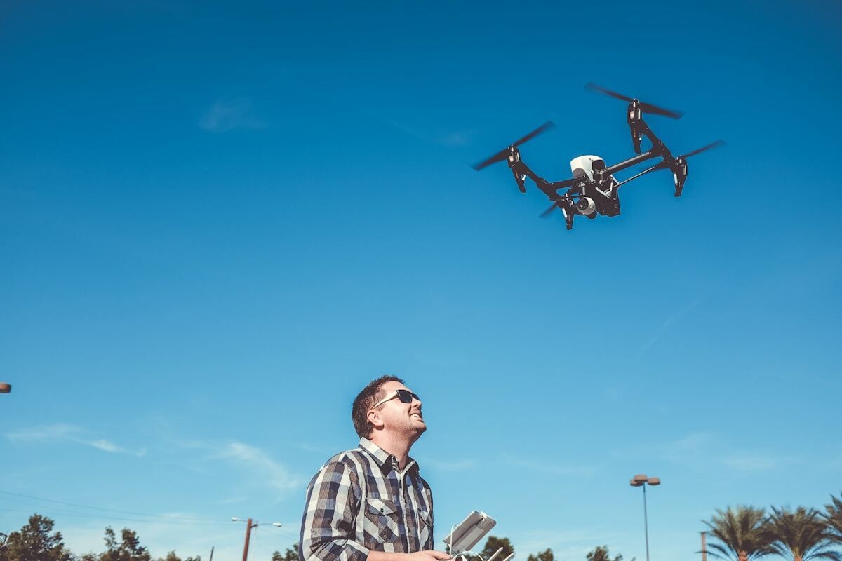 Homme en chemise à carreaux pilotant un drone volant dans le ciel bleu.