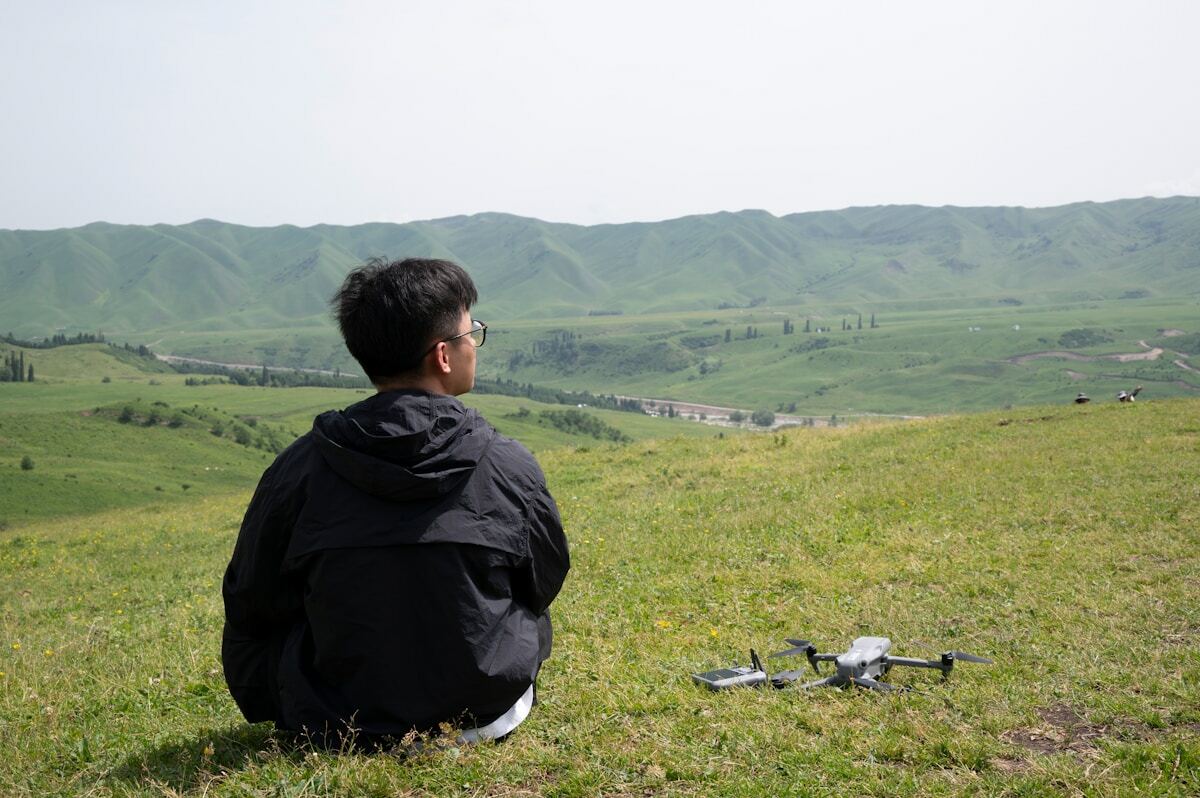 Homme observant le paysage montagneux avec un drone posé au sol.