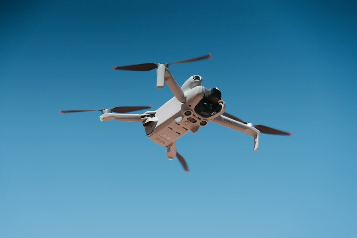 A white drone flying against a clear blue sky.