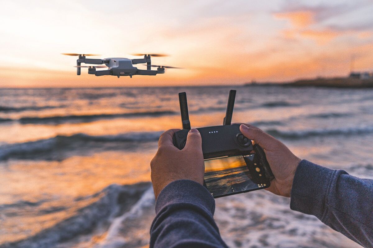 Drone volant au-dessus d'un coucher de soleil sur l'océan, contrôlé par une personne.