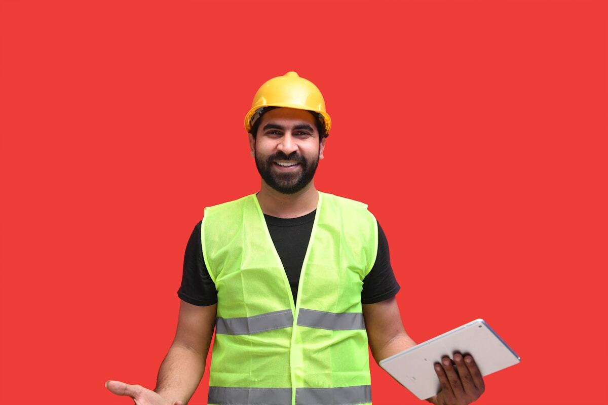 Un homme souriant portant un casque de sécurité et un gilet de sécurité jaune, tenant une tablette.