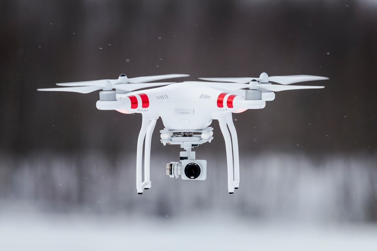 Drone blanc avec caméra survolant un paysage enneigé.