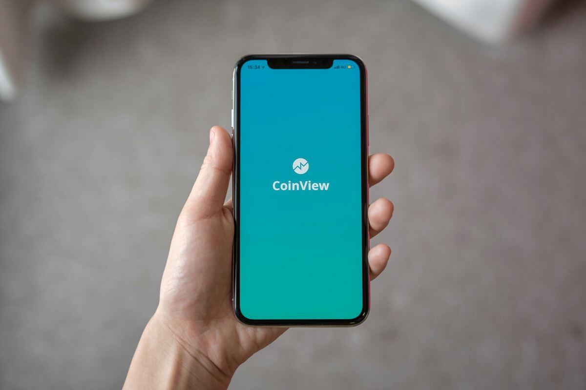 Smartphone affichant l'application CoinView avec un écran bleu turquoise.