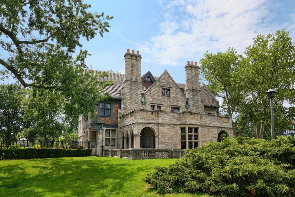 Manoir historique en pierre avec cheminées, balcons et jardin verdoyant.