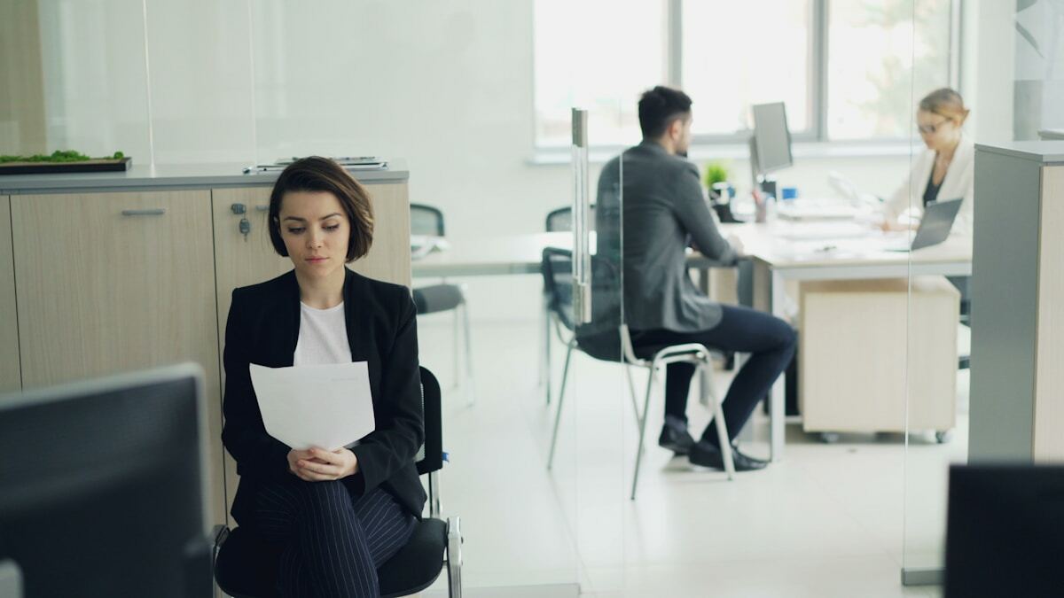 Femme en costume noir attendant dans un bureau moderne.