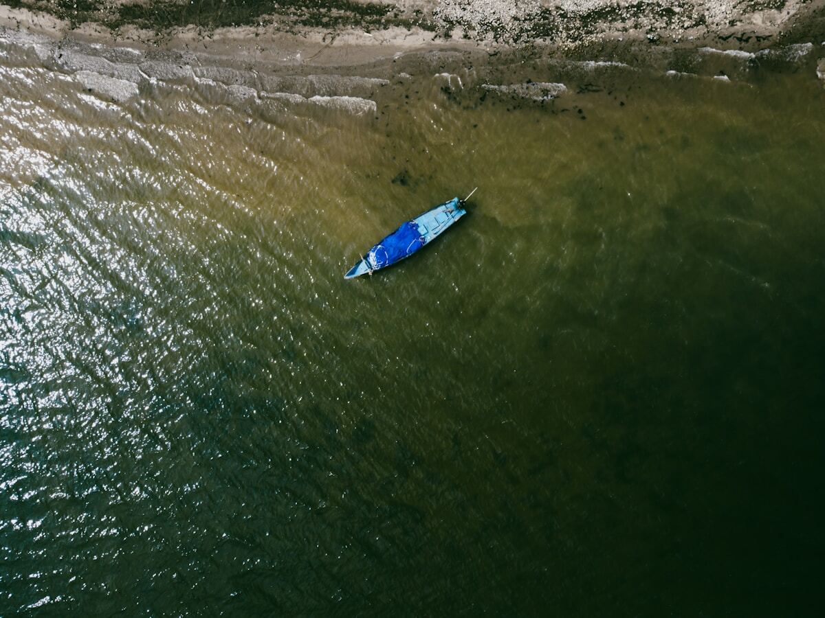 Bateau bleu solitaire naviguant sur une eau verte et ondulée.